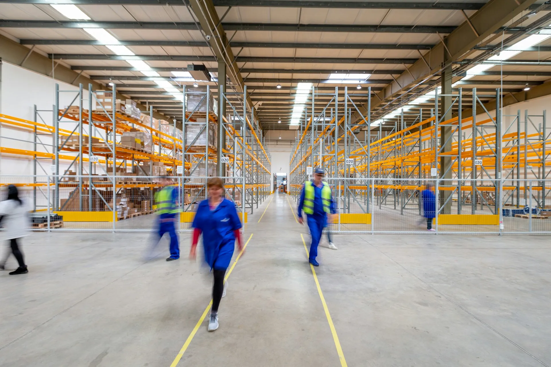Spacious warehouse interior with workers, shelving units, and organized aisles.