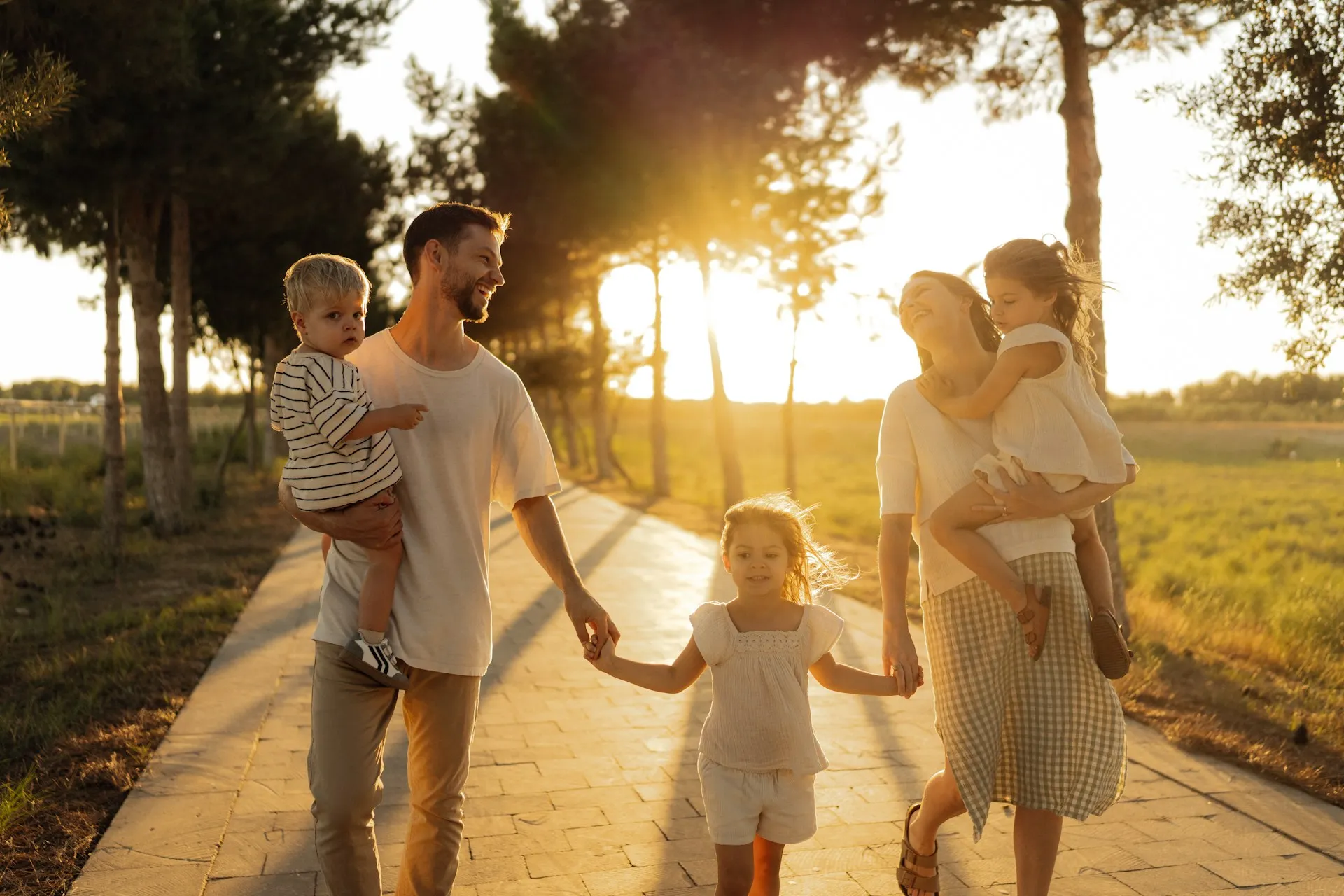A happy family walking together on a path during sunset, with children being carried and holding hands.