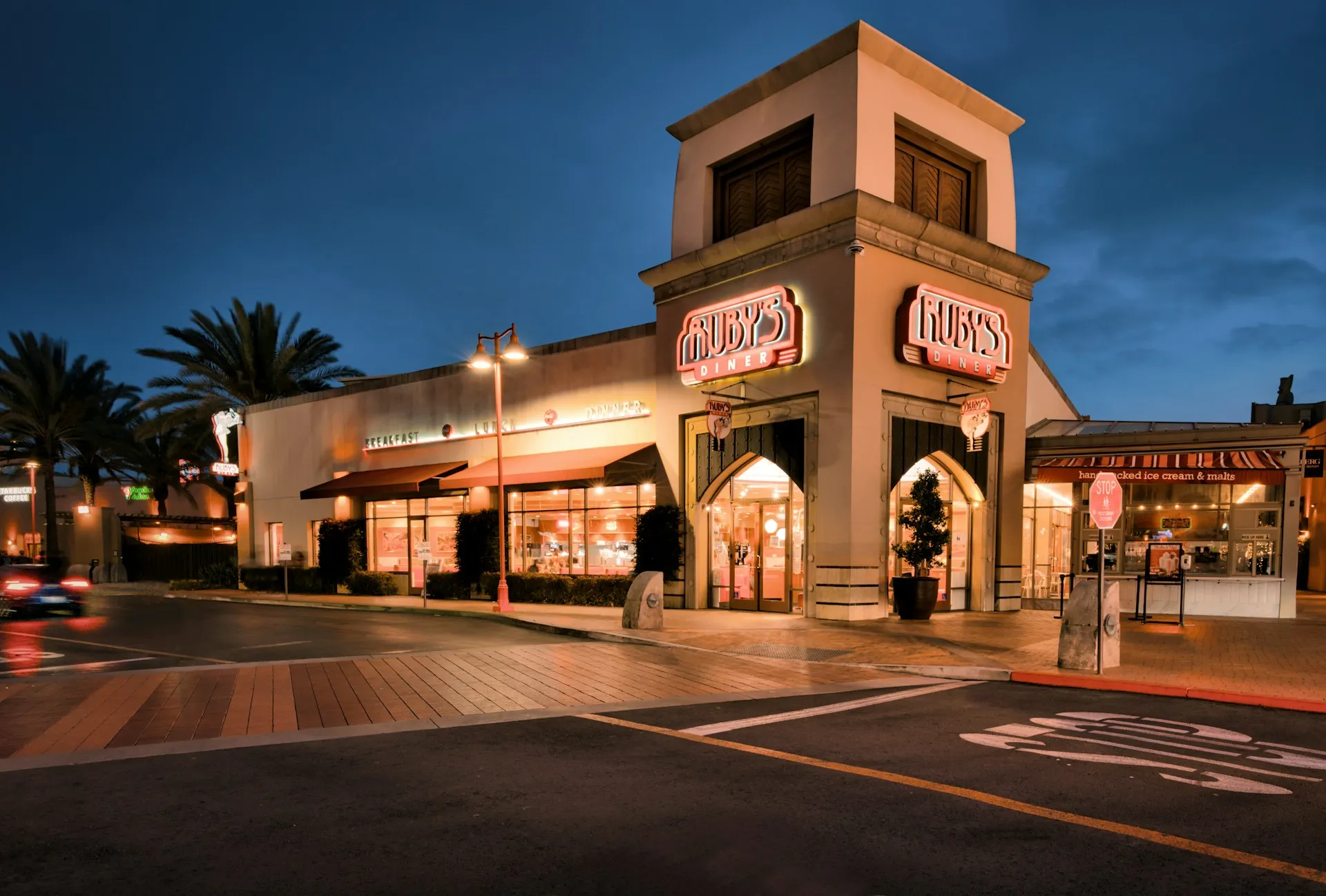 A restaurant building named Ruby's at dusk, with palm trees and a street in the foreground.
